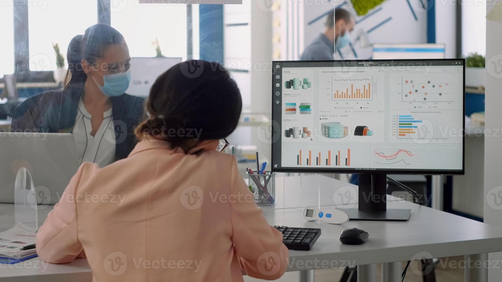 Business woman talking at phone with partners while team working in background in company office during coronavirus lockdown. Coworkers keeping social distancing to avoid virus disease photo