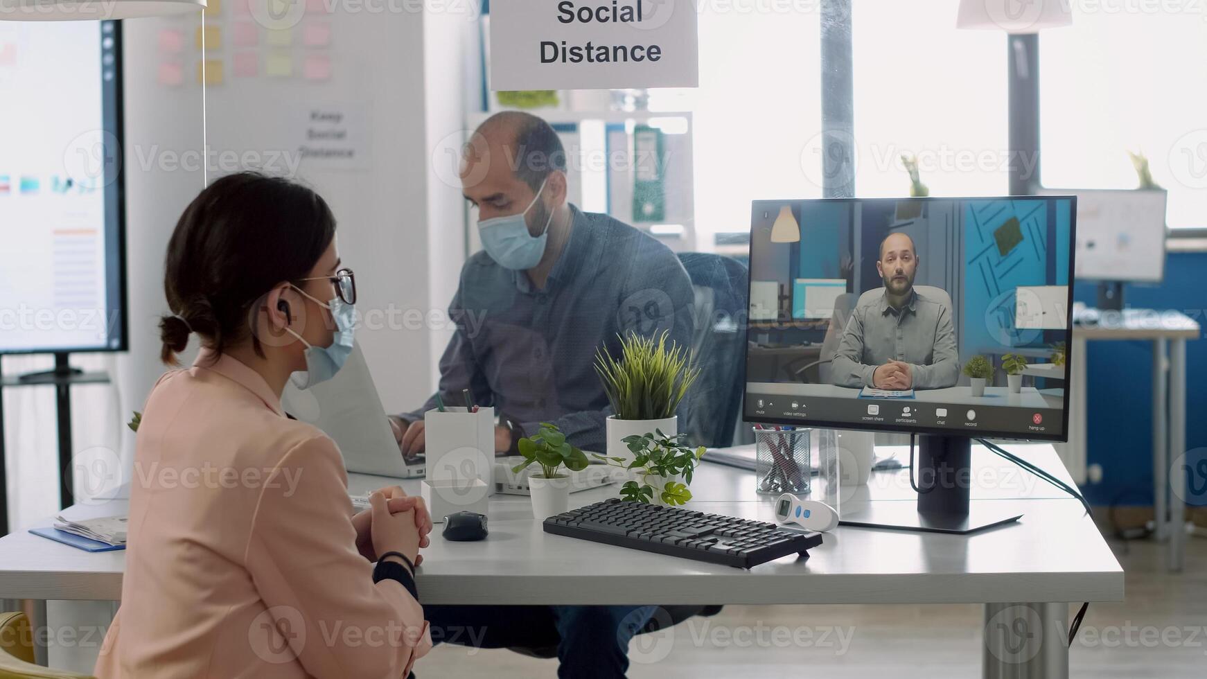 Freelancer with protective face mask talking with collegue during virtual videocall conference while sitting in business office. Coworkers respecting social distance to prevent infection with covid19 photo