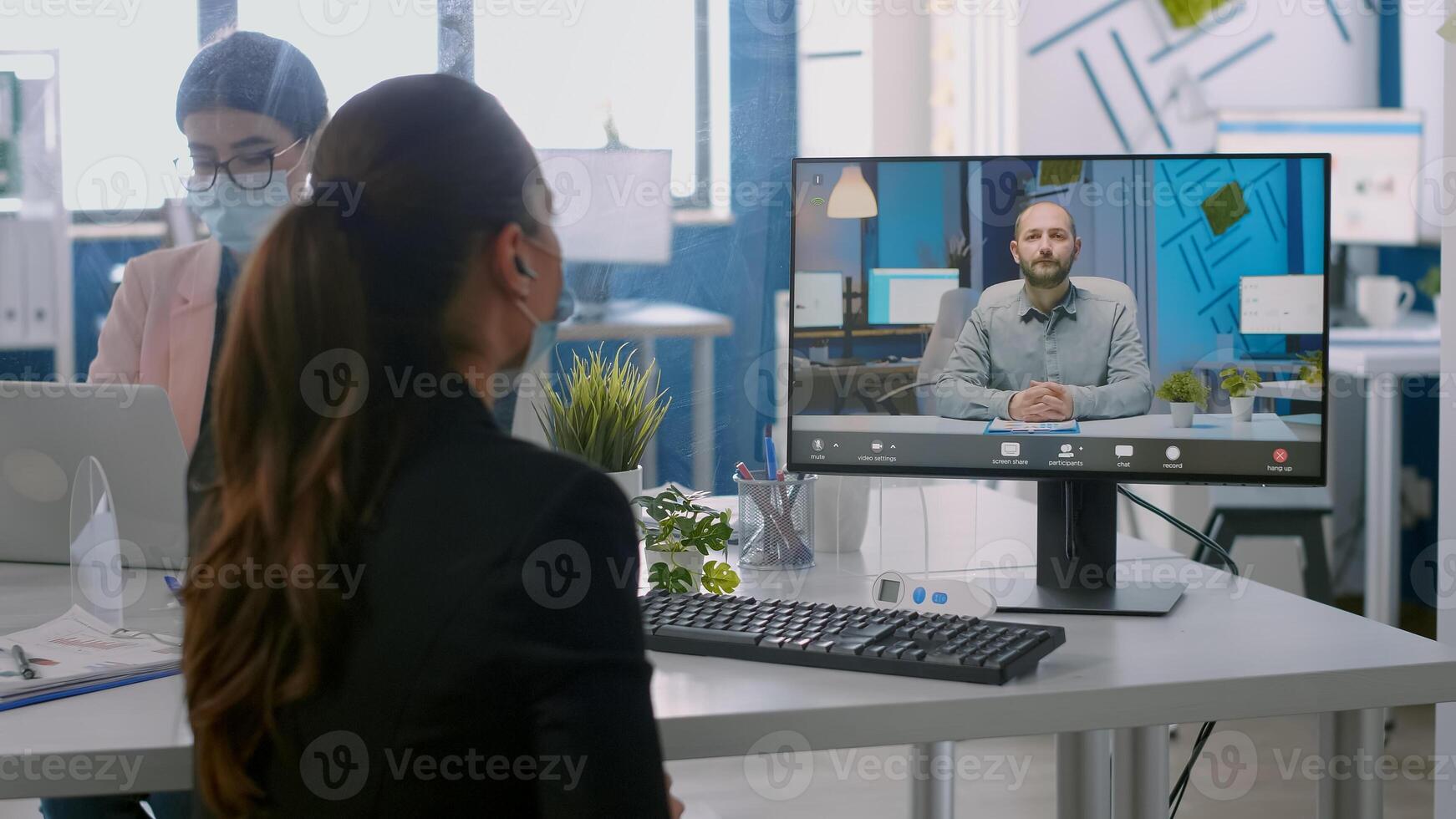 Back shot of businesswoman wearing medical face mask talking on videocall meeting with remotely team. Executive freelancer working in new normal company office during coronavirus pandemic photo