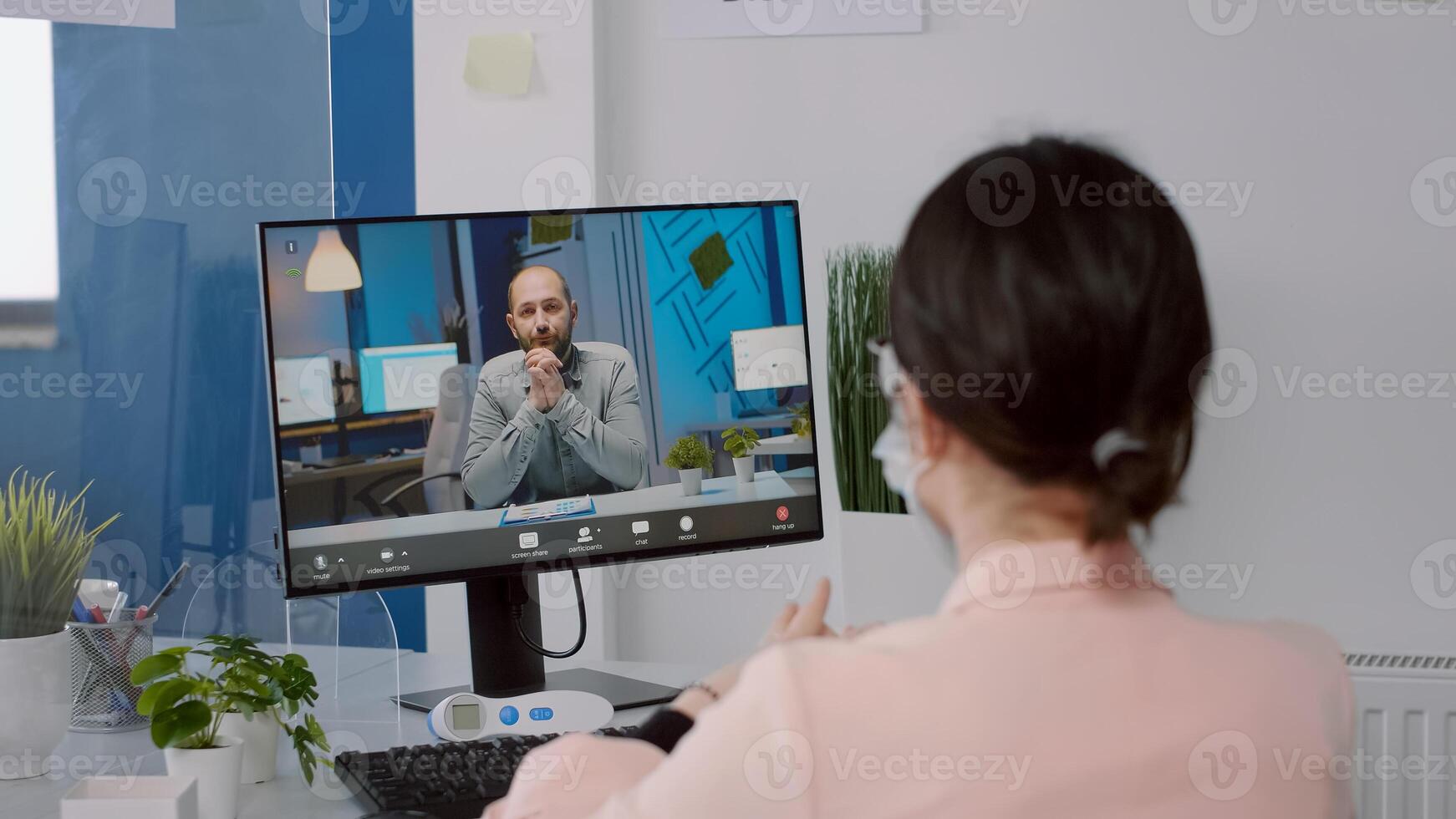 Freelancer with protection face mask talking with executive manager on computer duringvirtual meeting while sitting in new normal business office. Caucasian female working during coronavirus pandemic photo