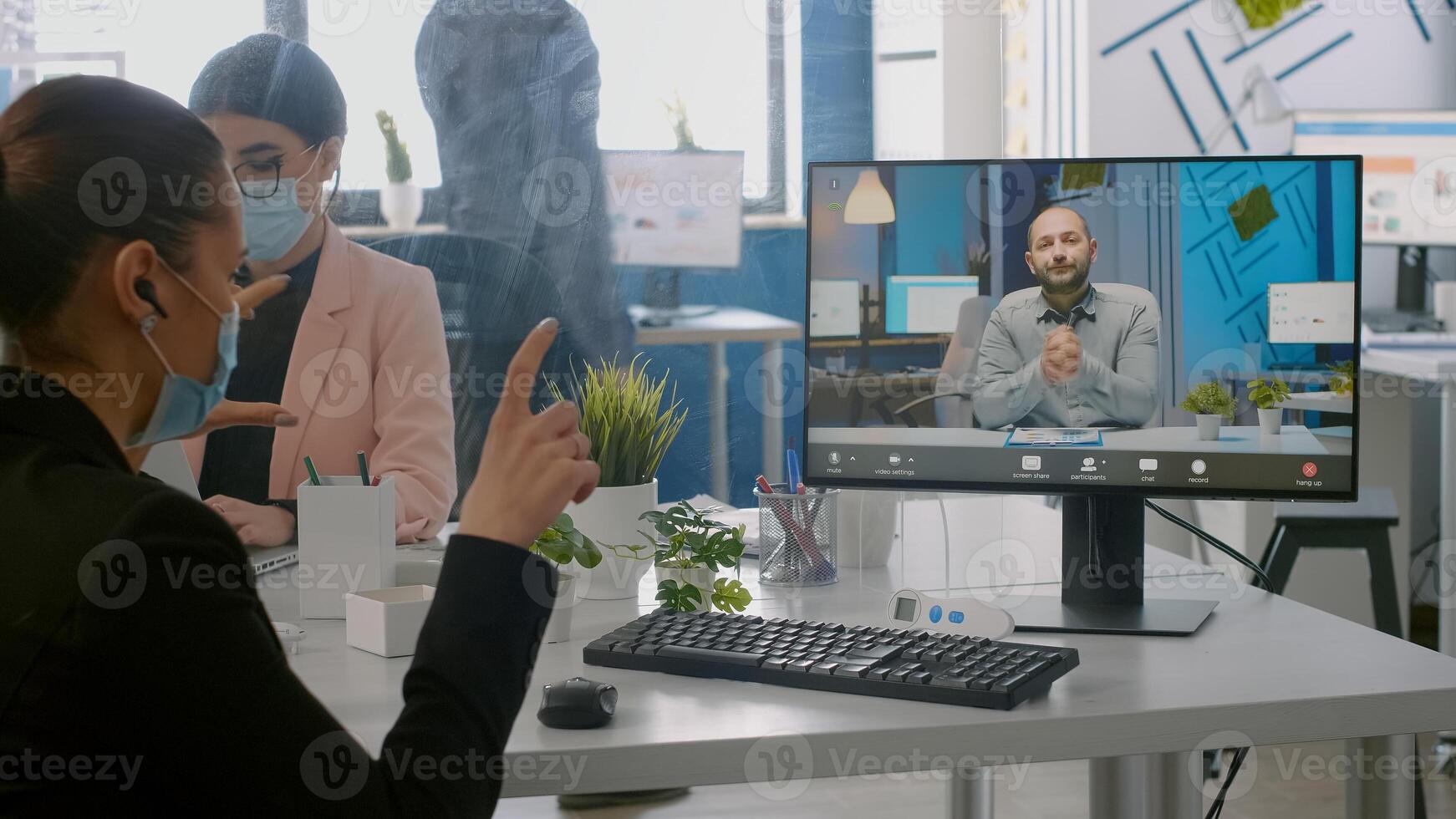 Freelancer wearing protective face mask during online videocall sitting at desk in startup company office. Coworkers working on computer during coronavirus global pandemic photo