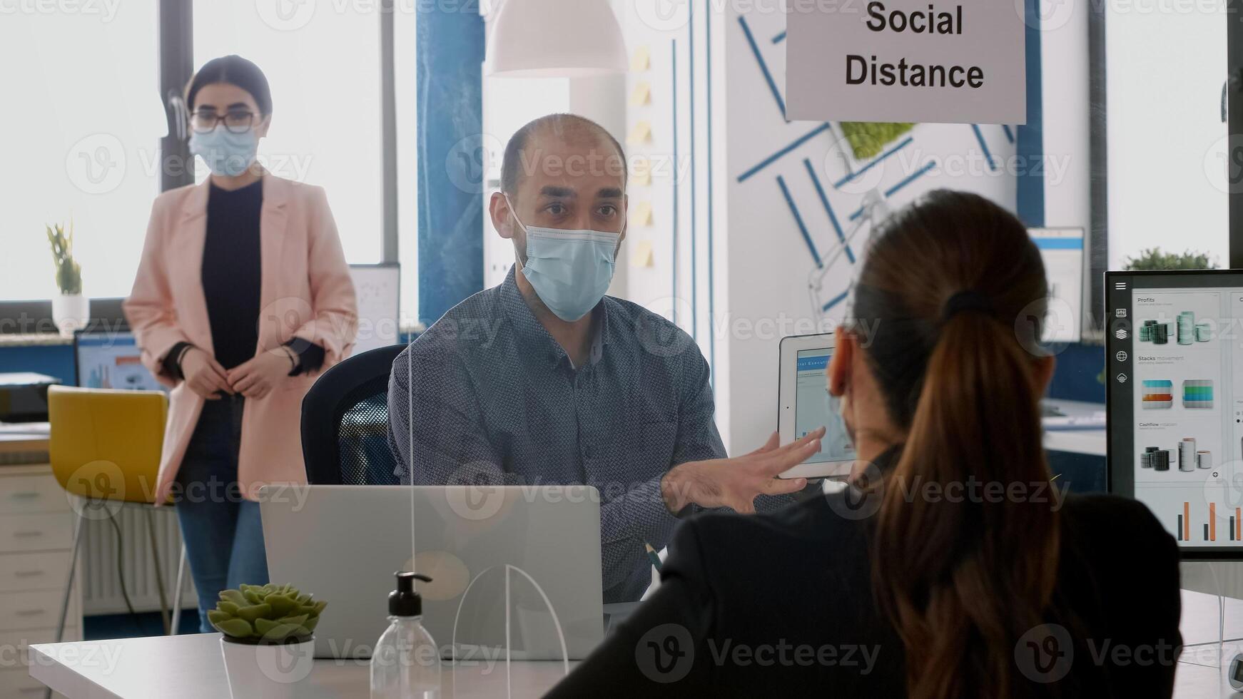 Two collegues with face masks working at marketing project using tablet computer while sitting in company office . Business team keeping ing ing social distancing to avoid infection with coronavirus photo