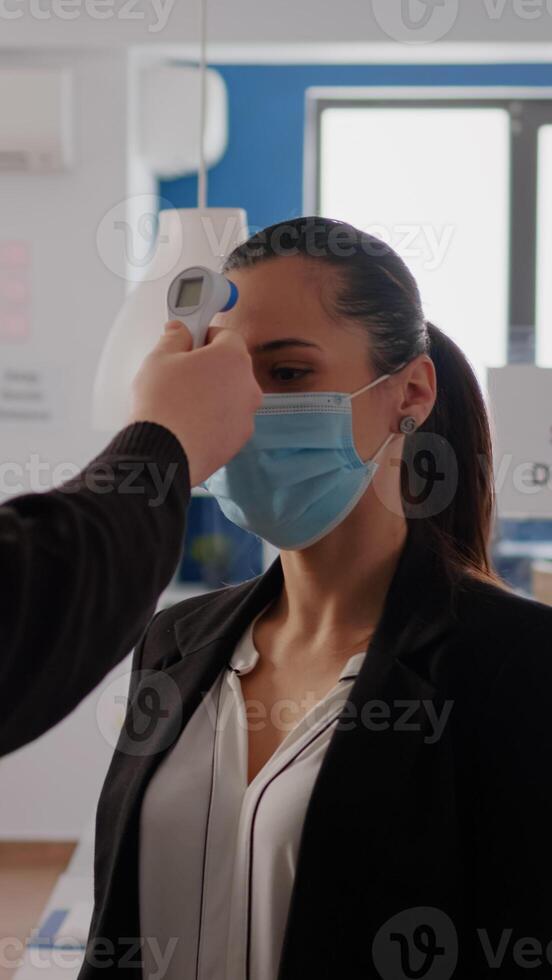 Business man with protective face mask checking collegues temperature using infrared thermometer to prevent virus infection. Coworkers keeping social distance to prevent coronavirus spread photo