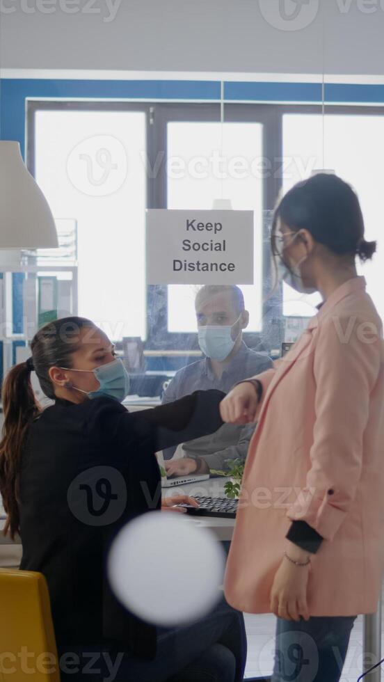 Two coworkers touching elbow during coronavirus global pandemic while working at business project wearing medical face mask to prevent infection with virus disease. Company mantain social distancing photo