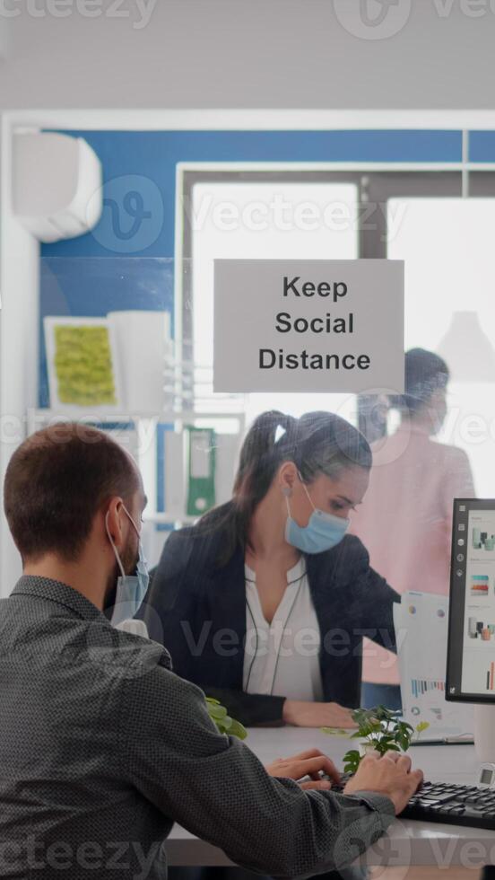 Businesspeople analysing financial graphics while working after lockdown in new business office wearing protective face mask to prevent infection with coronavirus. Team mantain social distancing photo