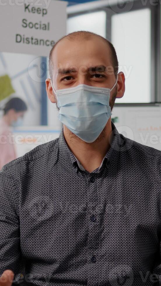 Pov entrepreneur man with protective face mask during zoom meeting call in new normal office. Freelancer talking into camera on remote online conference call photo