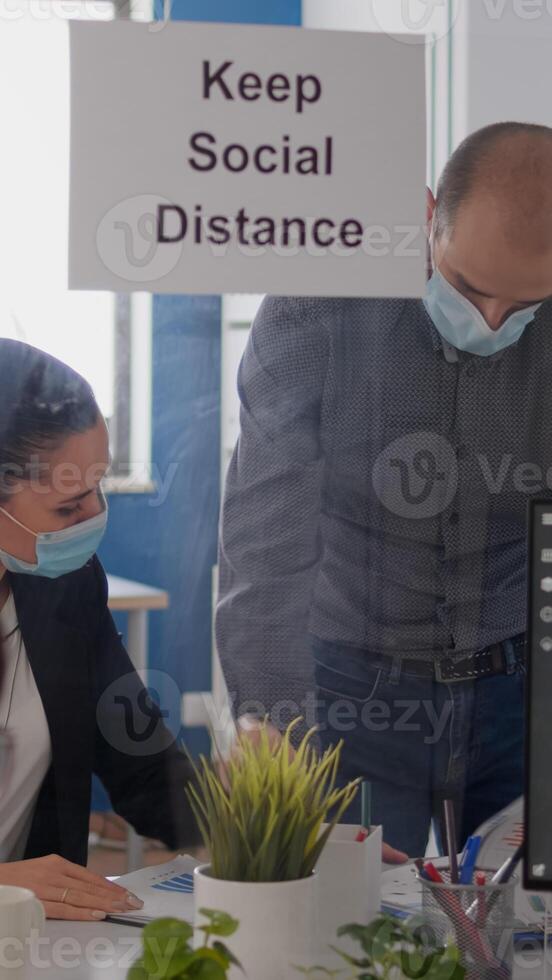 Business people with medical face masks sitting in new normal company office analysing financial project during covid19 pandemic. Coworkers keeping social distancing to avoid virus disease photo