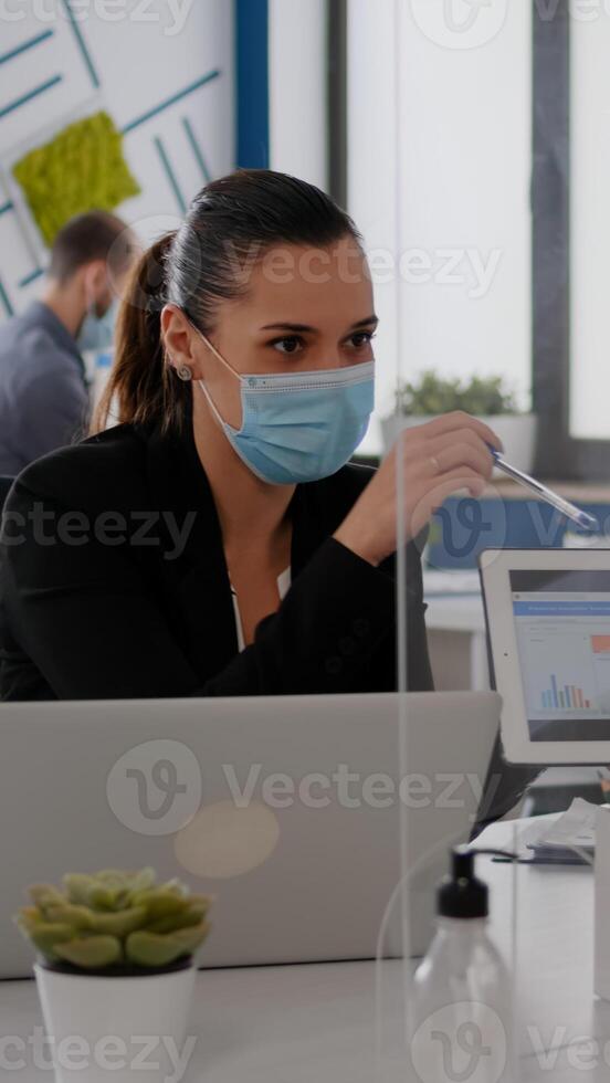 Close up of coworkers with face mask working together at financial project using tablet computer while sitting in company office. Team mantain social distance to avoid infection with covid19 photo