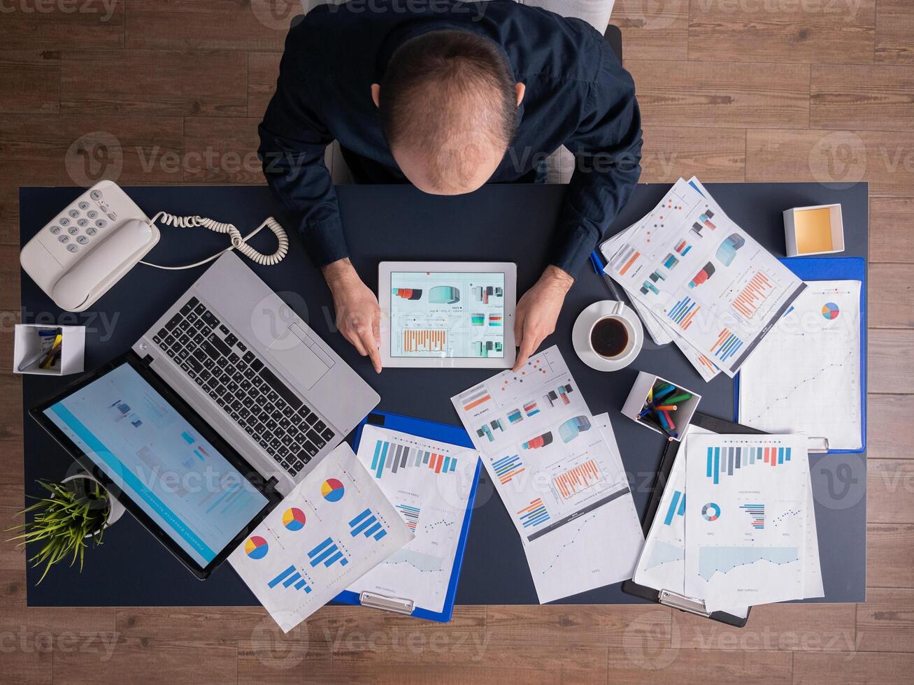 Top view of businessman using tablet pc analyzing financial charts and documents, sitting at desk in corporate office. Employee scrolling through graphs. Successful entrepreneur analyzing strategy. photo
