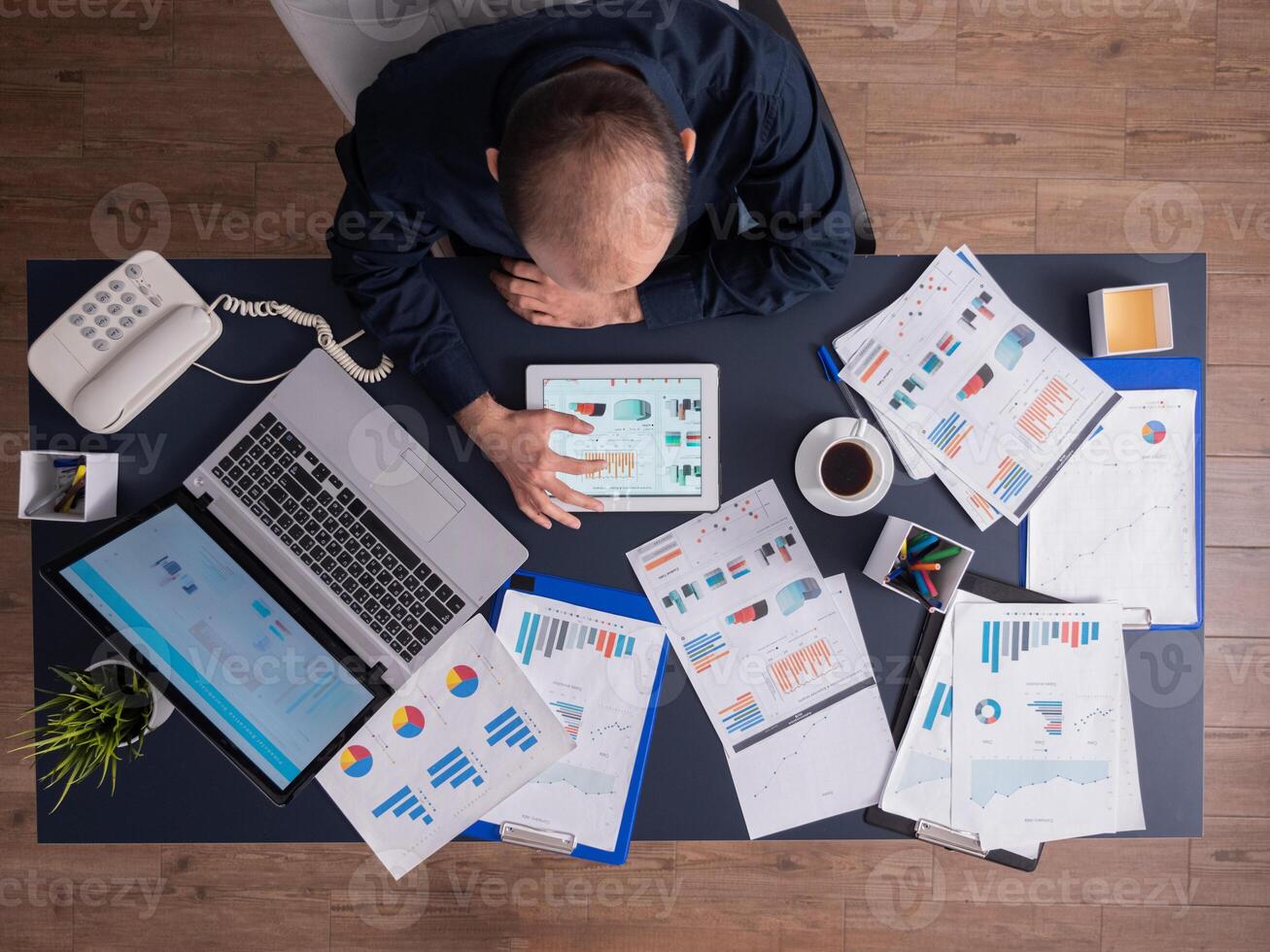 Top view of businessman using tablet pc analyzing financial charts and documents, sitting at desk in corporate office. Employee scrolling through graphs. Successful entrepreneur analyzing strategy. photo