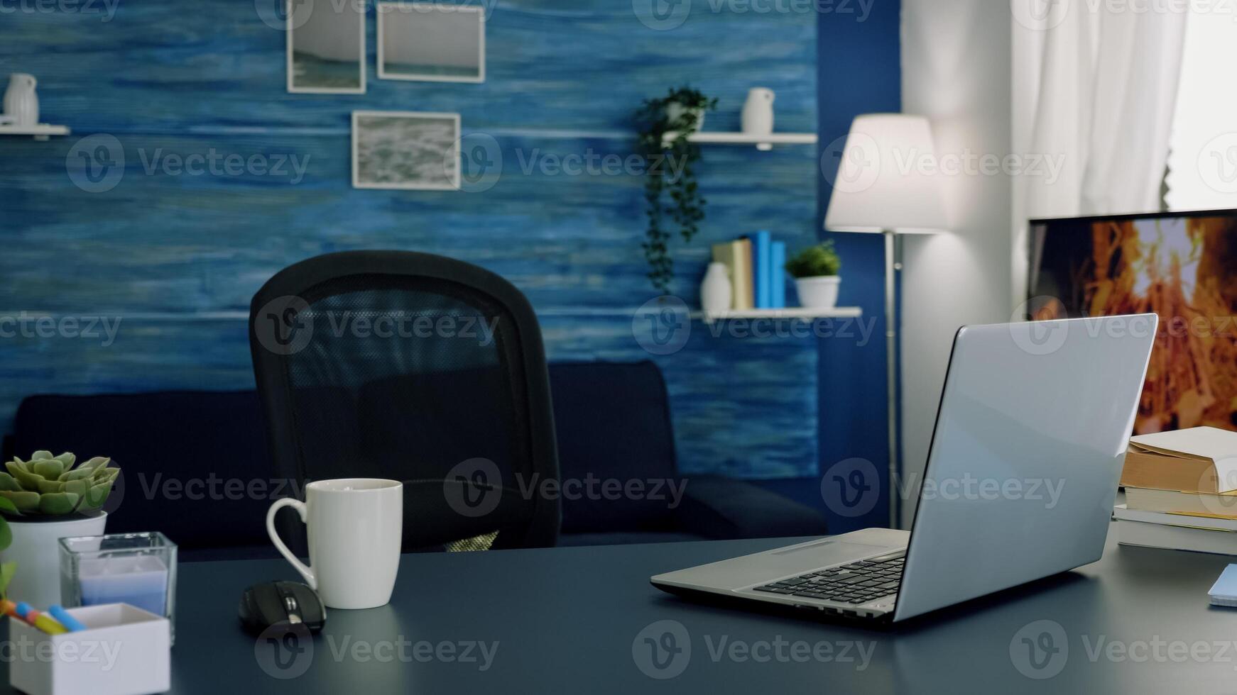 Pretty simple modern decor of cozy apartment with no people in it and television in background. Empty workspace of freelancer worker with laptop computer on desk and cup of coffee. photo