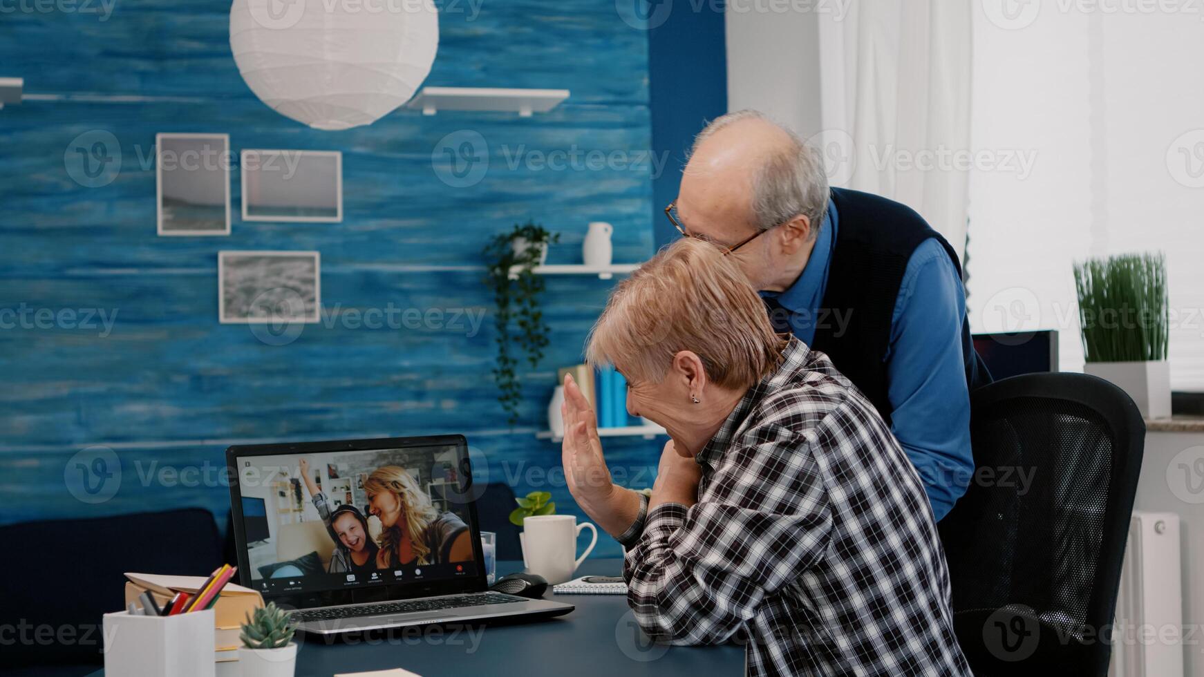 Happy senior couple waving during conference with nephews using laptop in living room. Elderly person using internet online chat technology webcam making virtual meeting call photo