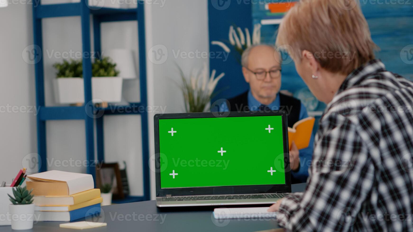 Elderly person reading on green screen, mock up, chroma key display of laptop, writing on notebook working from home. Senior woman watching at pc with isolated desktop, while man sitting on sofa photo