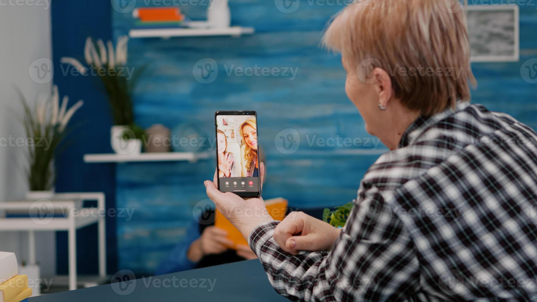 Senior woman having call online talk with nephew using smartphone sitting in living room. Retired granny using modern internet online tech to connect with grandparents photo