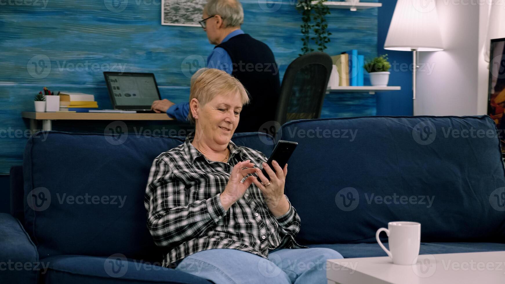 Happy middle aged mature woman enjoying using mobile apps texting typing messages sit on sofa, smiling old adult lady holding smartphone looking at cellphone screen browsing social media at home photo