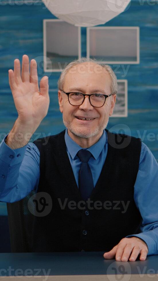 POV of elderly aged man waving during a conference with business partners working from home. Senior person using internet online chat technology webcam making virtual meeting call connection photo