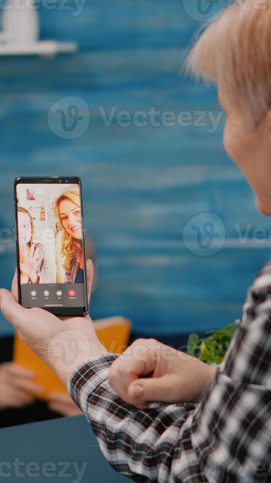 Senior woman having call online talk with nephew using smartphone sitting in living room. Retired granny using modern internet online tech to connect with grandparents photo