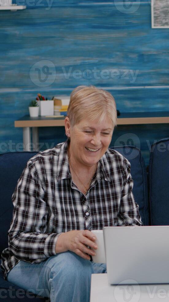 Happy senior couple waving at videocall with nephews using laptop sitting on couch in living room. Elderly person on internet online chat technology webcam, virtual meeting online conference photo