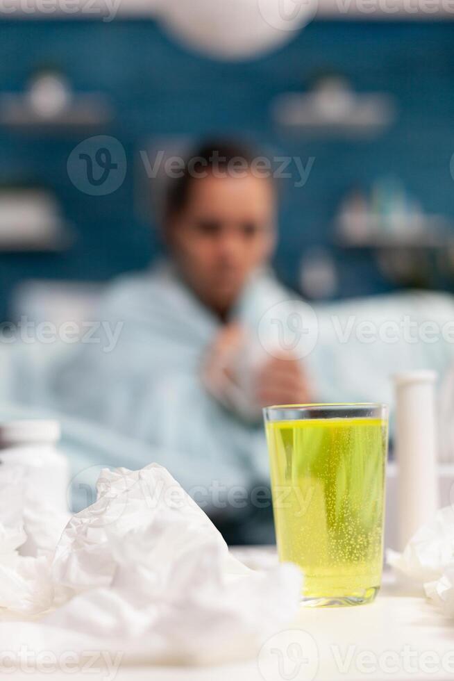 Cold young woman sitting at home on sofa with mug of tea against sickness disease illness. Caucasian person with temperature virus symptoms drinking warm vitamins from mug photo