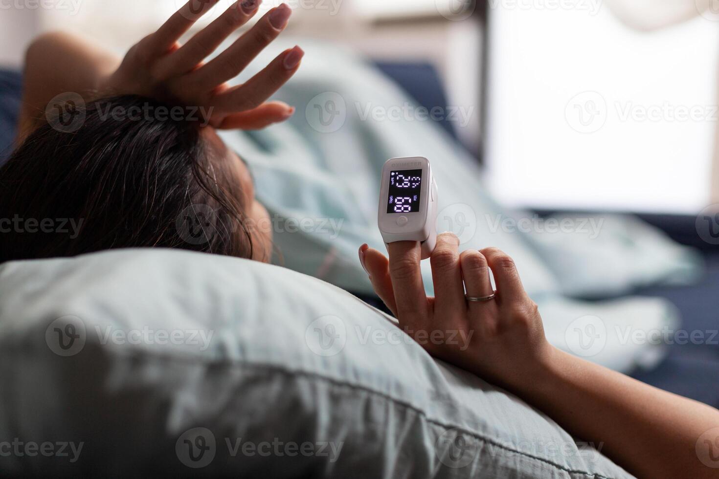 Woman at home using medical oximeter equipment to measure oxygen saturation. Pulse oximeter showing low oxygen saturation. Patient with covid in quarantine resting, measuring blood oxygen level. photo