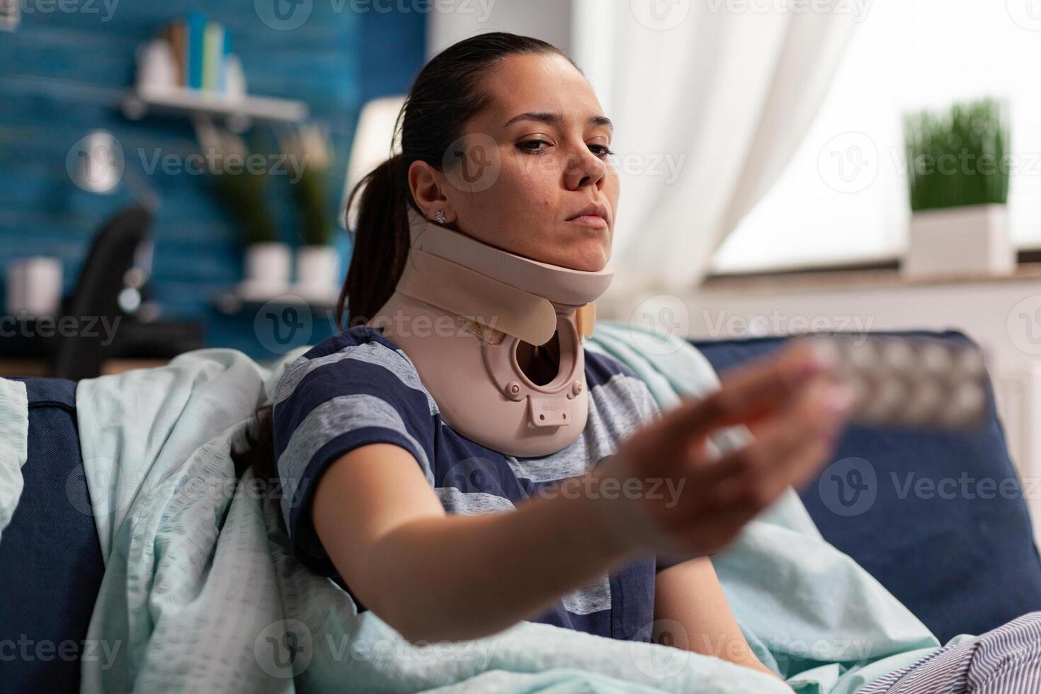 Woman with sickness and cervical foam collar on couch taking medical treatment for back and neck pain. Caucasian adult with muscular contracture after physical injury in accident photo