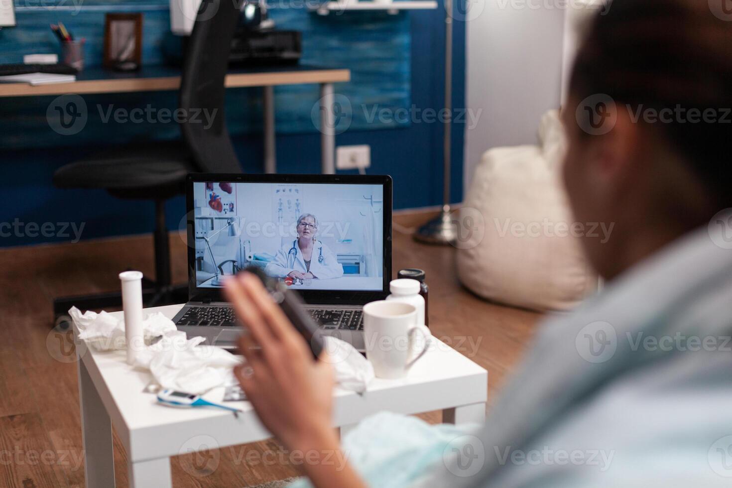 Cold young woman calling doctor from computer to treat flu illness virus fever temperature. Patient with thermometer on online consultation for treatment pills diagnostic assistance photo