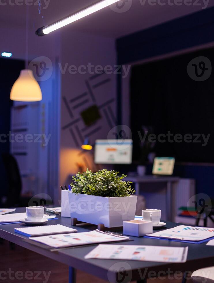 Modern empty business corporate office meeting room is ready for businesspeople late at night. In background on conference table standing company financial documents with economy graphs photo