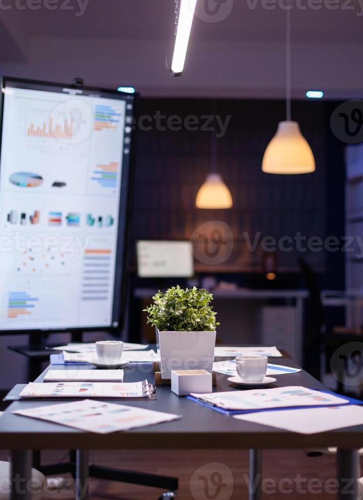 Empty business company office meeting room with nobody in it having presentation monitor with corporate statistics. On conference table standing financial graphs documents photo