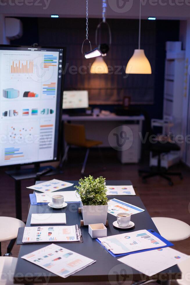 Empty business company office meeting room with nobody in it having presentation monitor with corporate statistics. On conference table standing financial graphs documents photo