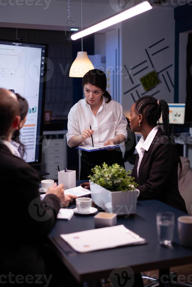 Entrepreneur woman brainstorming management strategy working hard in meeting office room late at night. Diverse multi-ethnic business team looking at financial company presentation on monitor. photo