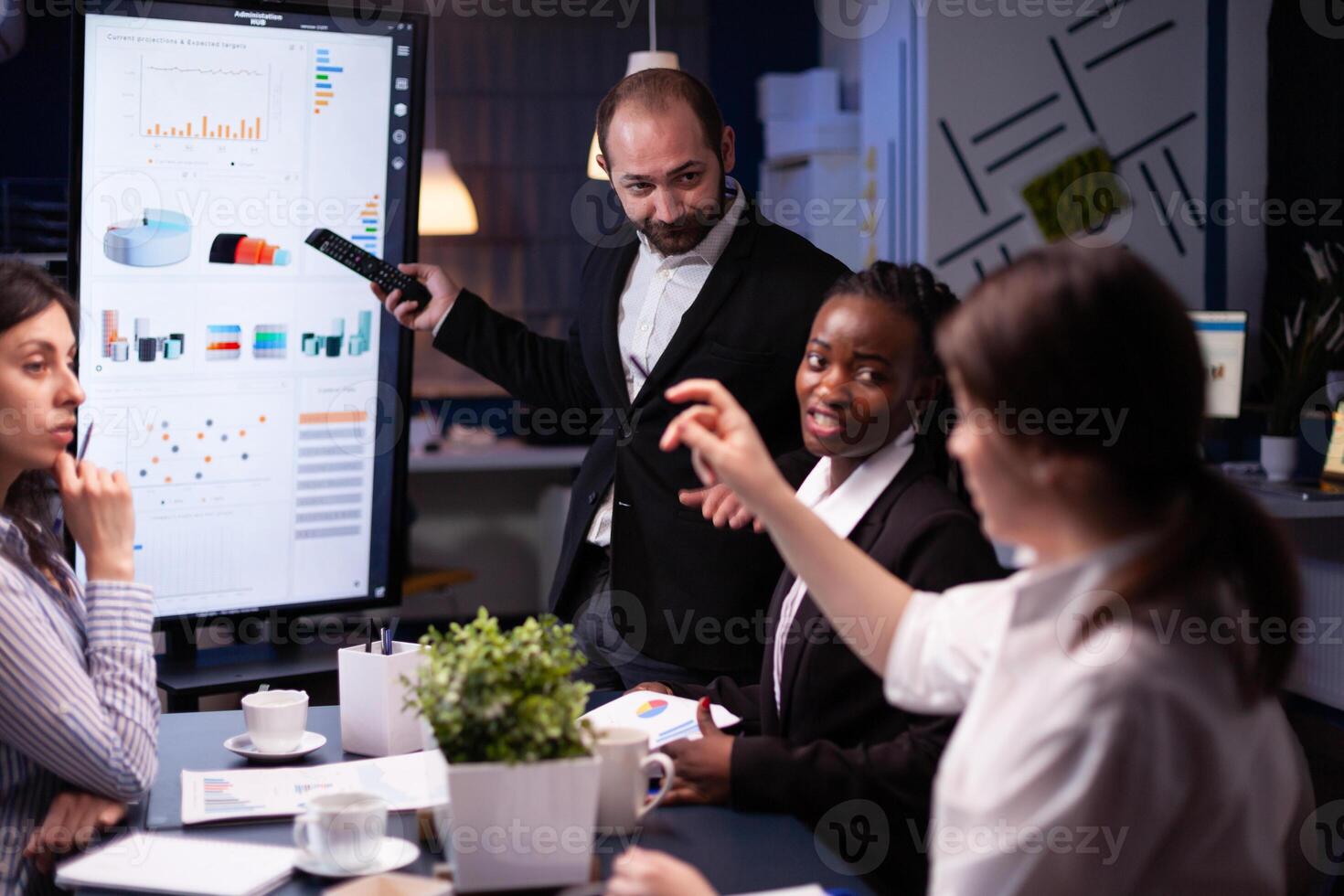 Entrepreneur man brainstorming management strategy working hard in meeting office room late at night. Diverse multi-ethnic business team looking at financial company presentation on monitor. photo