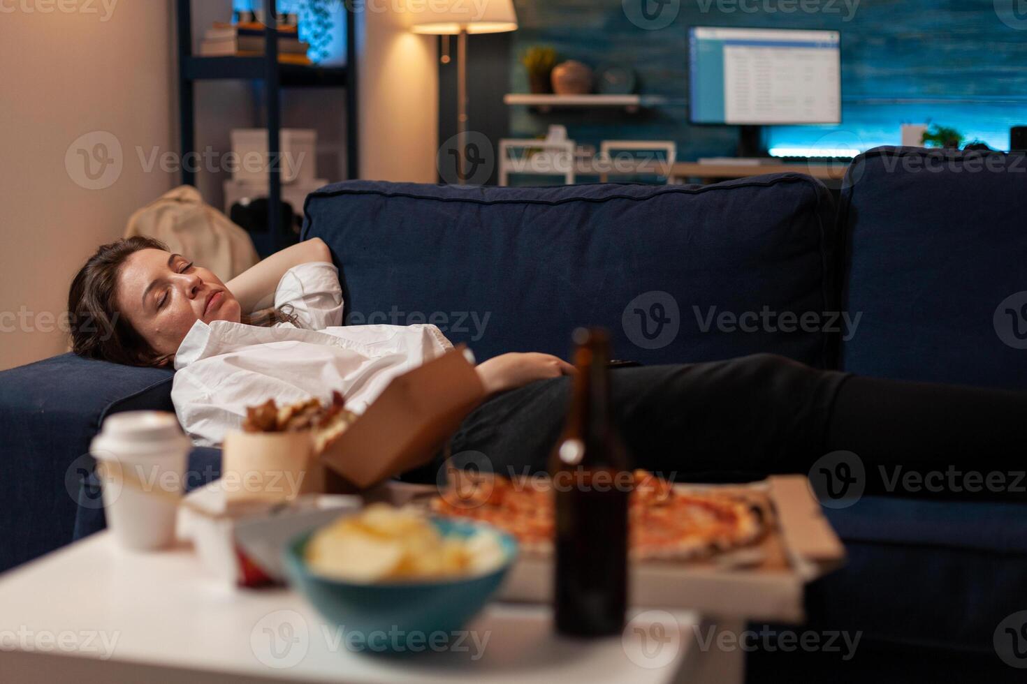 Person sleeping on sofa after drinking beer and eating home delivery pizza in front of television in living room. Tired woman falling asleep couch after large fast food takeout meal. photo