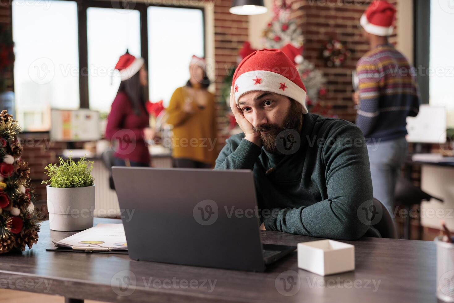 Exhausted startup company man employee working overtime for project deadline in office at christmas eve. Tired manager in santa hat having burnout in workplace during winter holiday photo