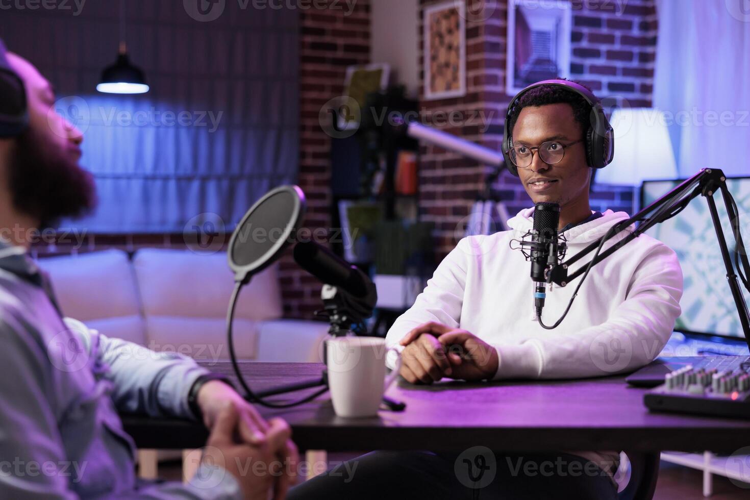 African american influencer recording podcast with guest, using professional equipment in home studio. Joyful men discussing live during broadcasting session for internet show photo