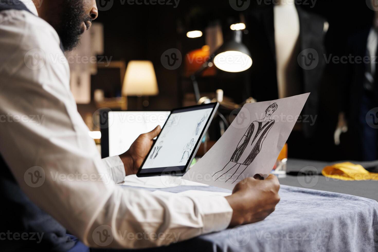 Dressmaker meticulously analyzing online sketch designs of fashion outfits displayed on tablet in tailoring studio. Tailor looking for inspiration for upcoming sartorial custom handmade collection photo
