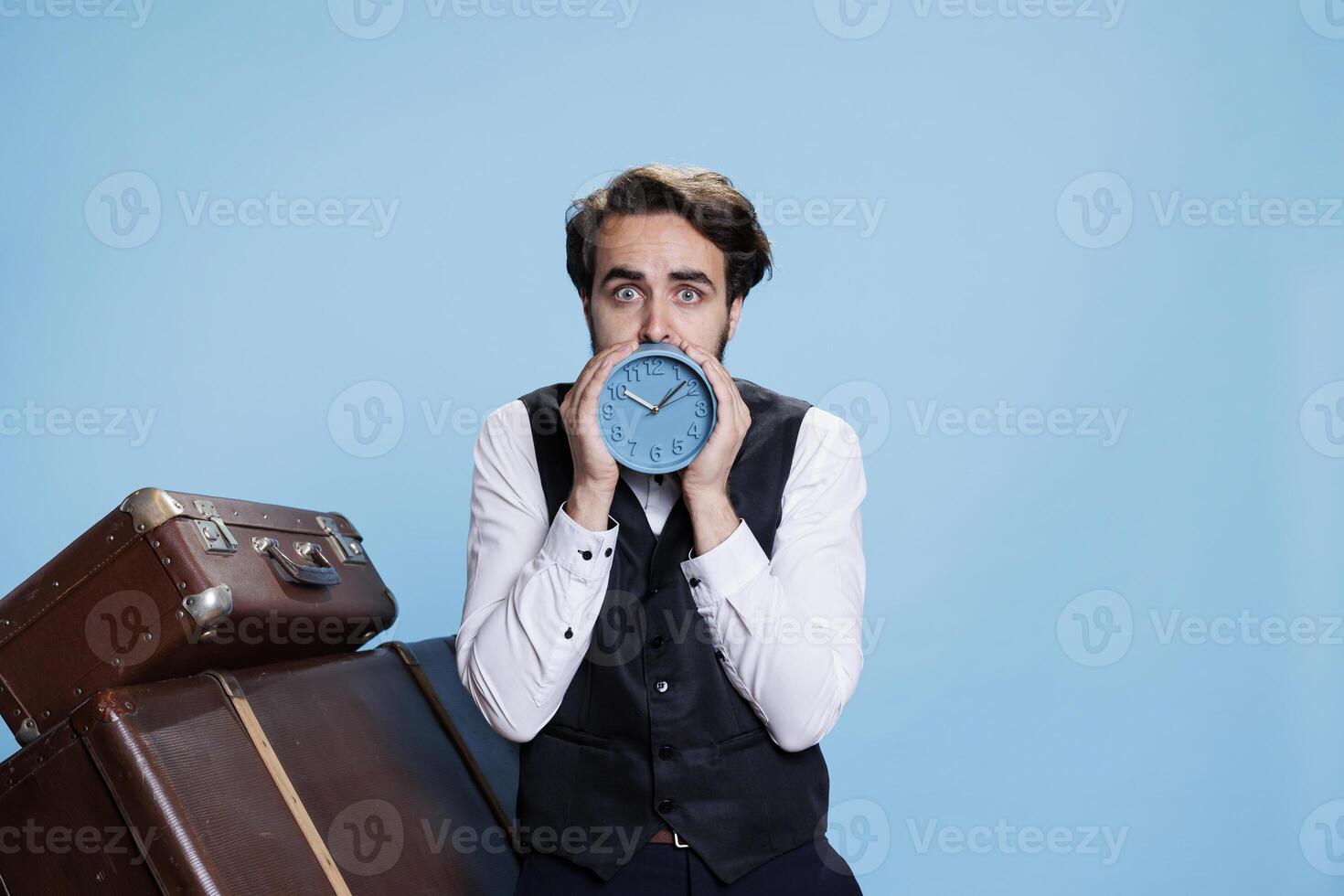 Hotel concierge checking time in studio, working as bellhop or doorman and holding wall clock to look at hour. Young adult in formal attire posing with watch, trying to be punctual. photo
