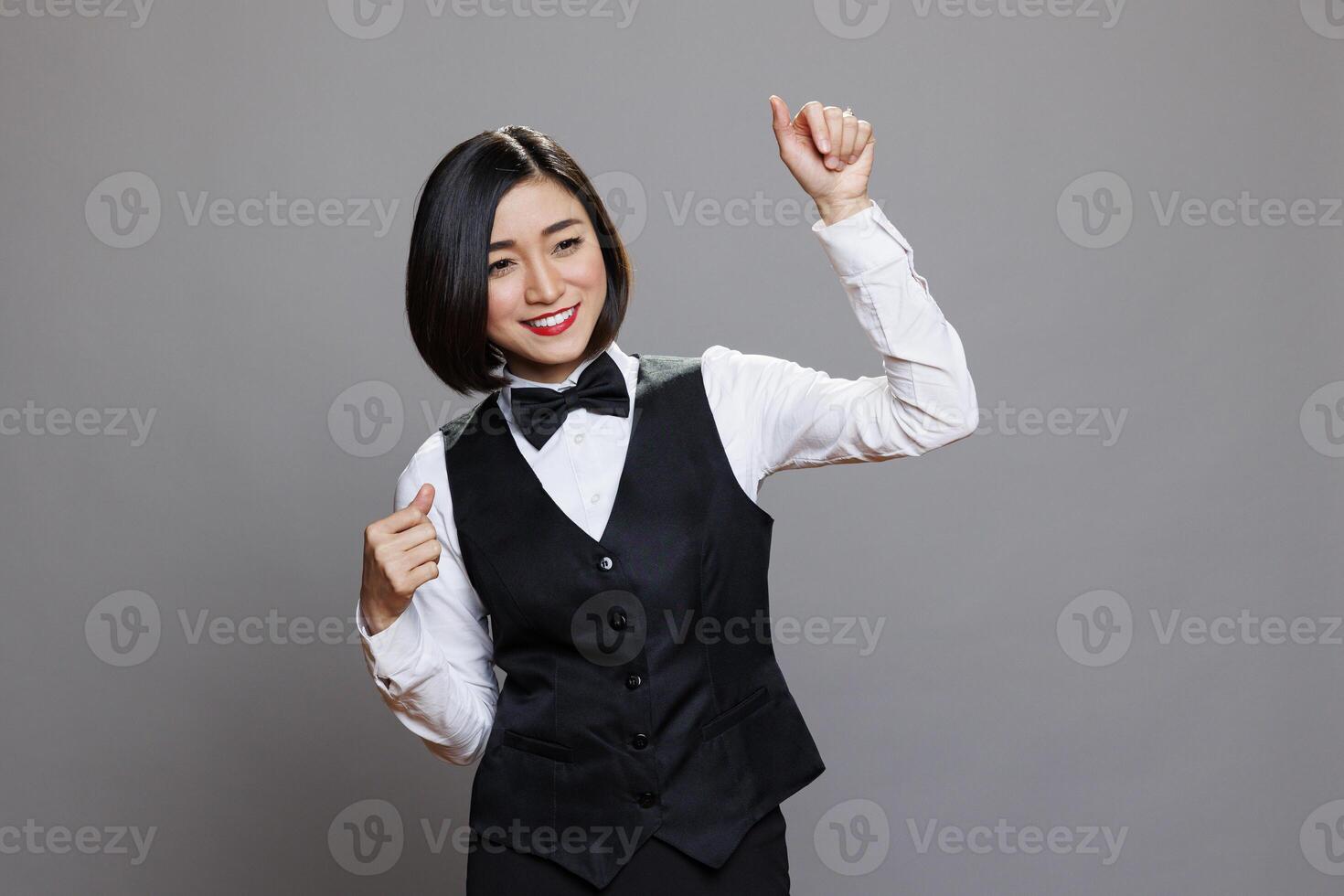 Restaurant cheerful smiling asian waitress dancing, raising hands with positive facial expression. Carefree relaxed attractive woman receptionist moving to music rhythm in studio photo