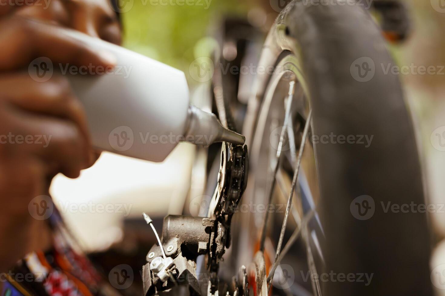 Young african american female cyclist diligently cleaning and greasing her bike pedal for optimal performance. Close up woman doing bicycle maintenance ensuring top-notch service and smooth ride. photo