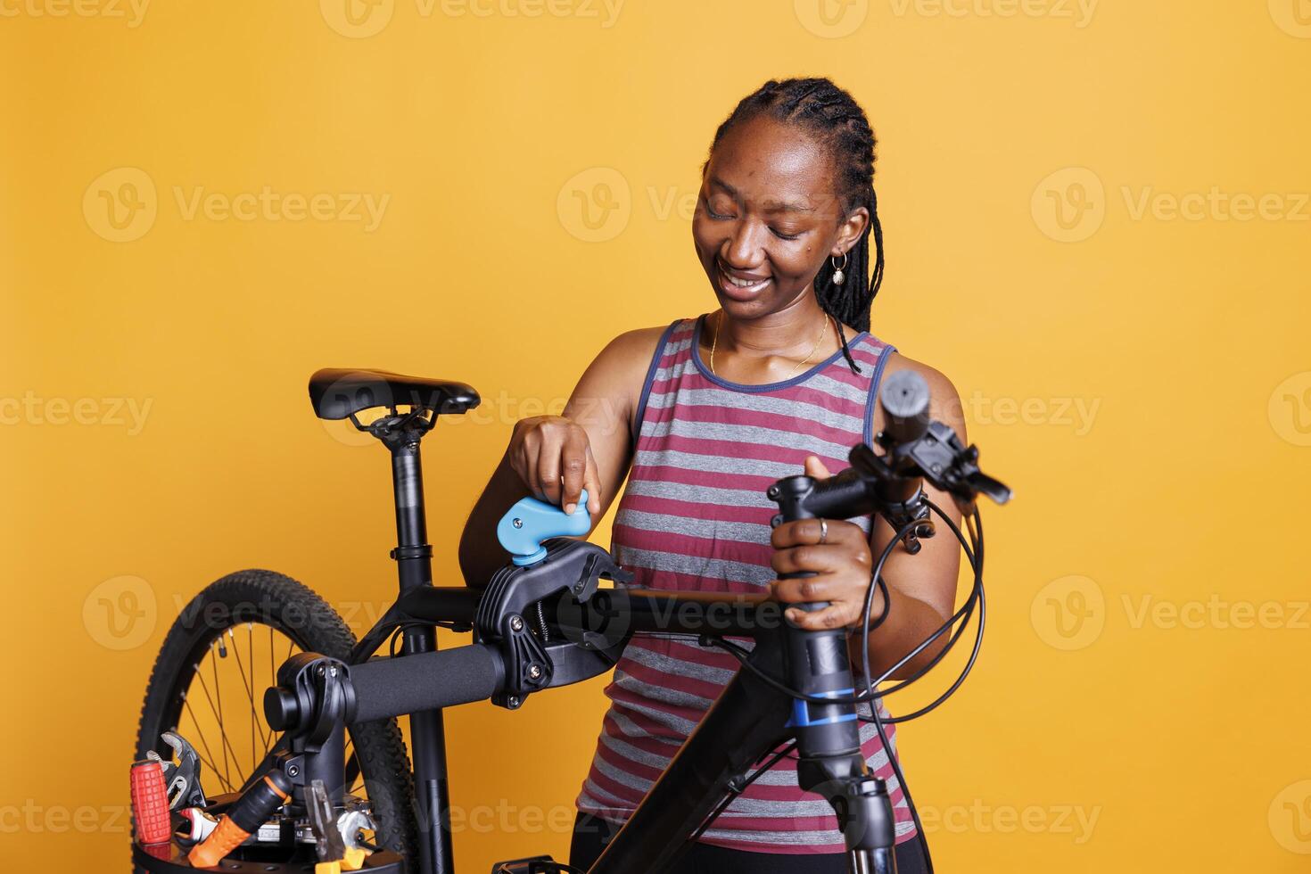 African American woman who enjoys sports looks at a repair stand for a bicycle frame that has to be fixed. Young black woman with a smile clamps and secures damaged bike for inspection and repair. photo