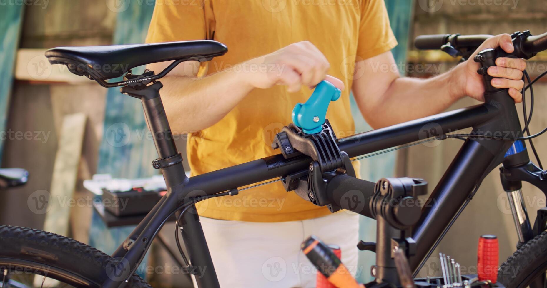 Closeup shot of young man securing and fastening bike frame to specialized repair-stand for maintenance in yard. Detailed view of person carefully realigning and adjusting bicycle for servicing. photo