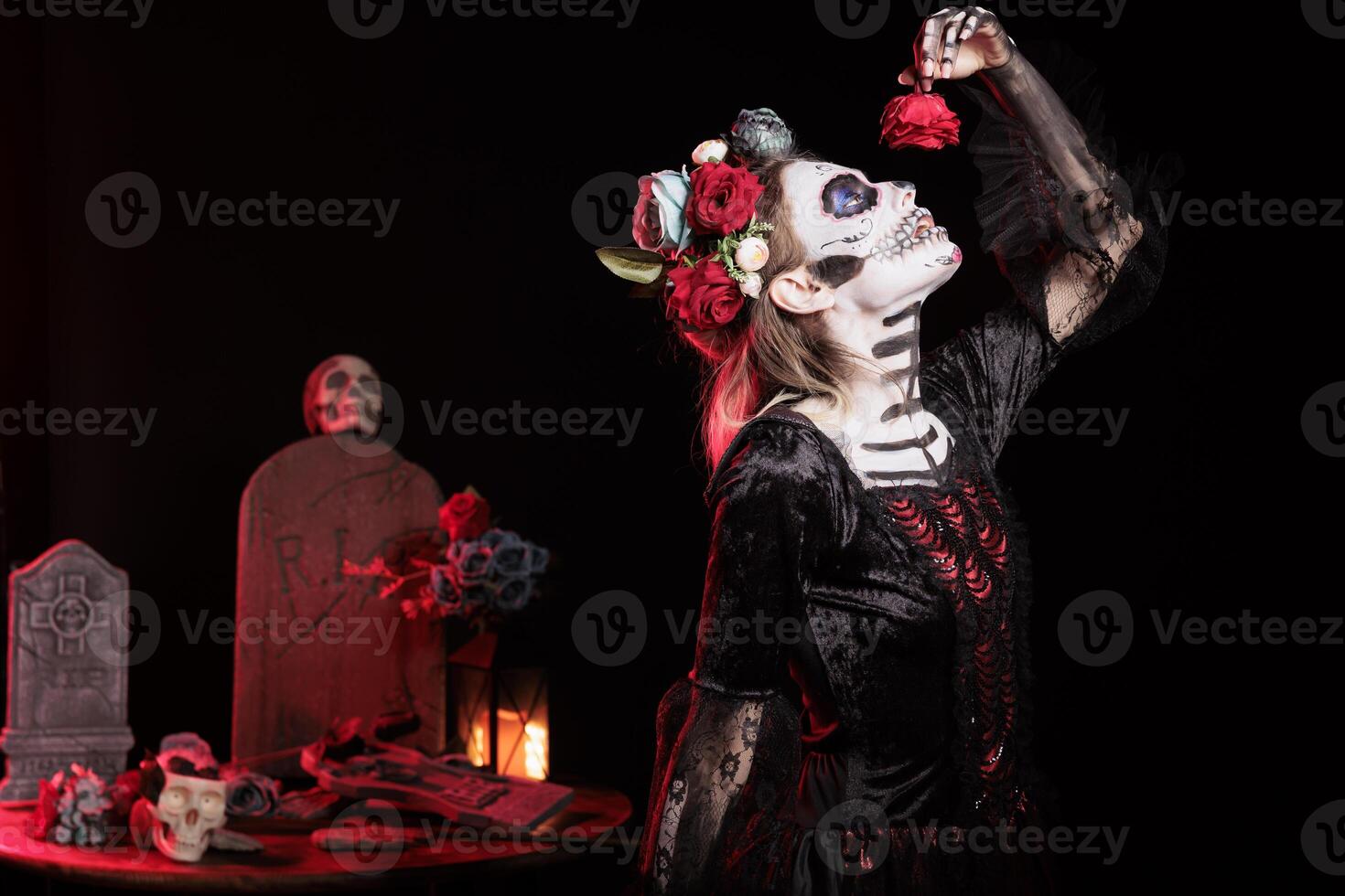 Woman posing for Day of the Dead Mexican celebration honoring dead loved ones, pretending to eat red rose. Goddess lady doing ancient Aztec custom of celebrating ancestors, devouring flower photo