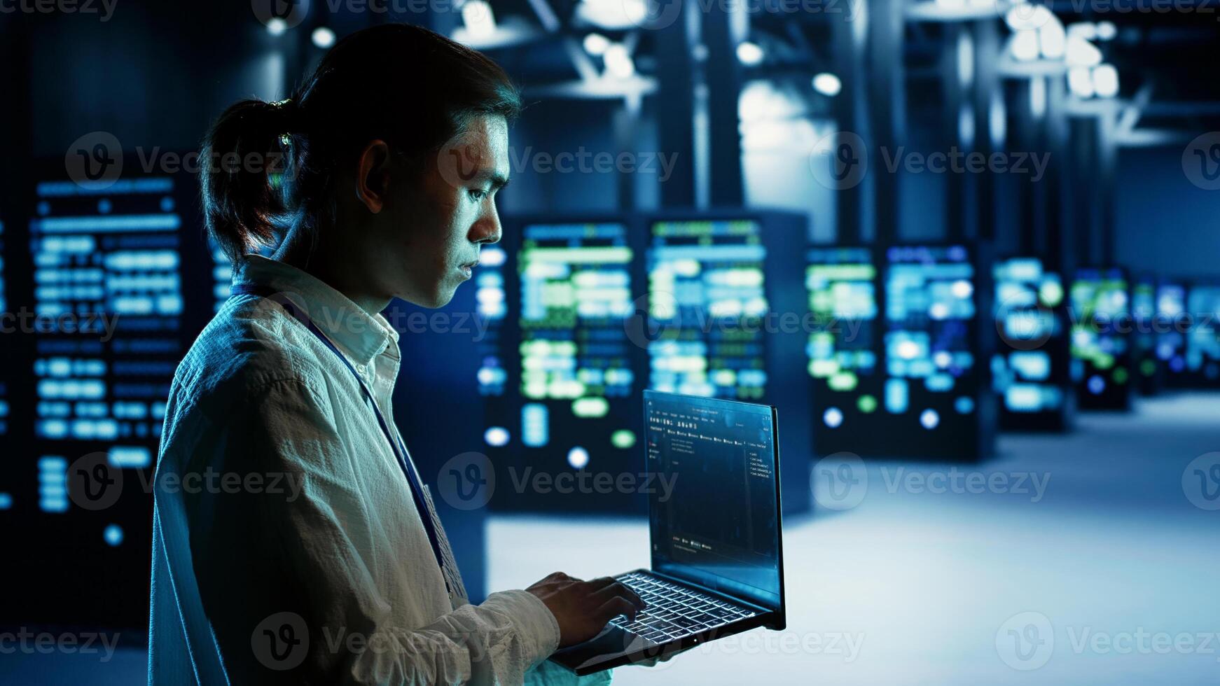 Certified asian technician running code on laptop, maintenancing and upgrading data center equipment designed to accommodate server rows, networking systems and storage arrays photo