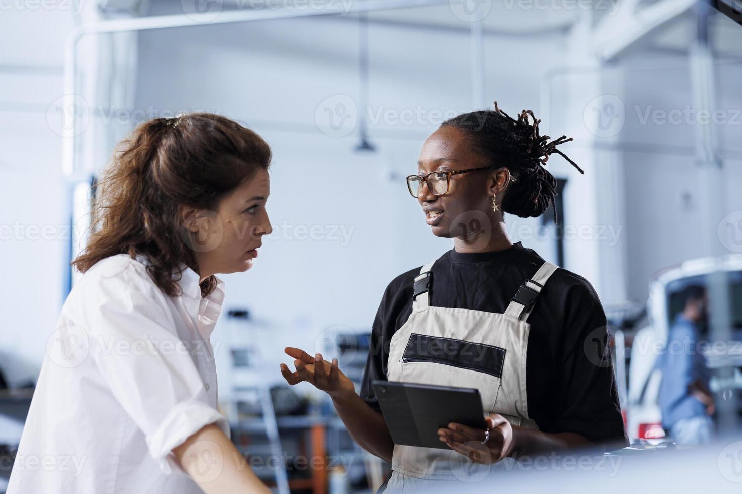 Meticulous mechanic at auto repair shop conducts annual vehicle checkup, informing client about needed engine replacement. Garage specialist talks with customer after finishing car inspection photo