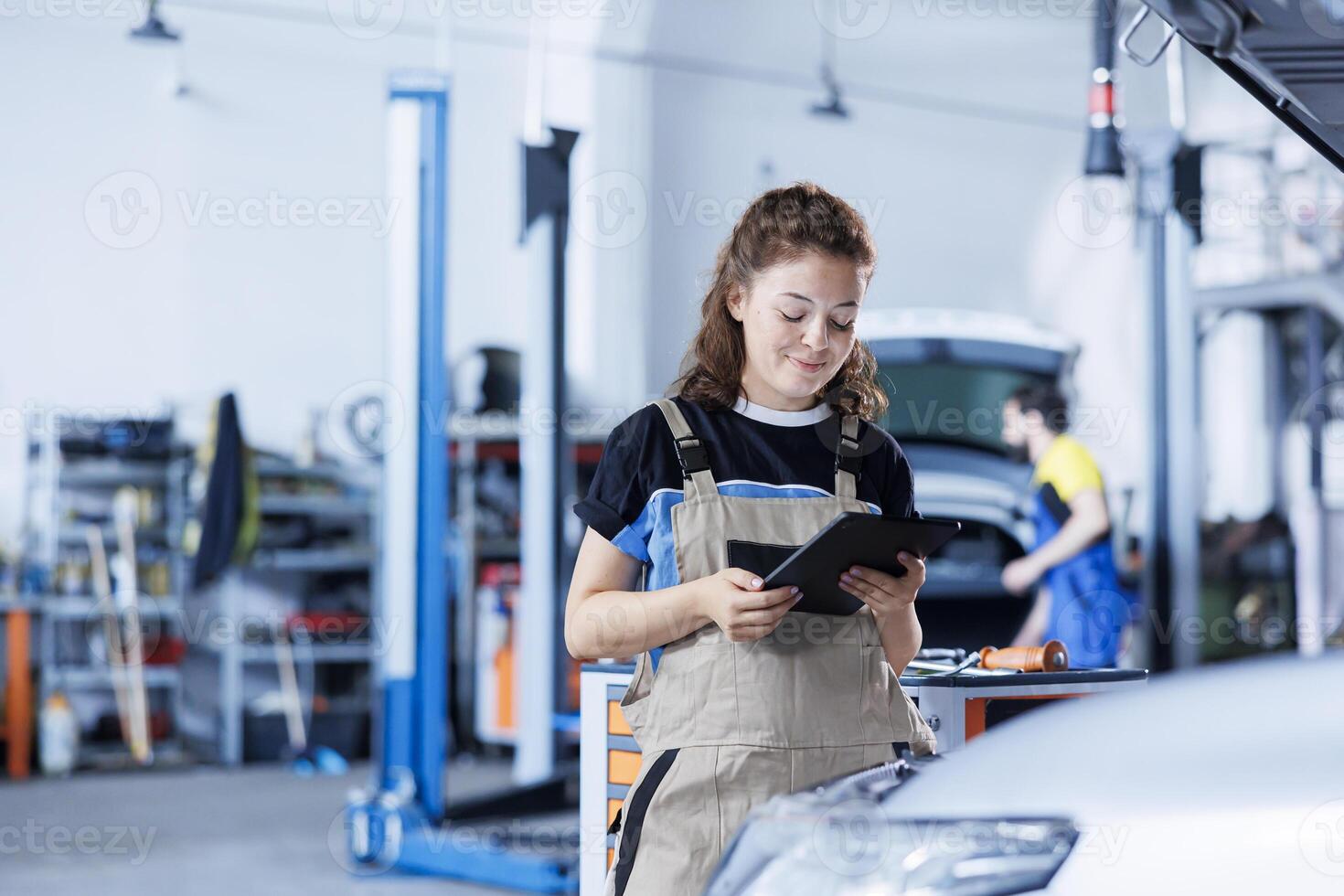 Technician in car service uses tablet to calculate invoice for client after repairing steering mechanism. Experienced expert in garage calculating final costs after servicing customer vehicle photo