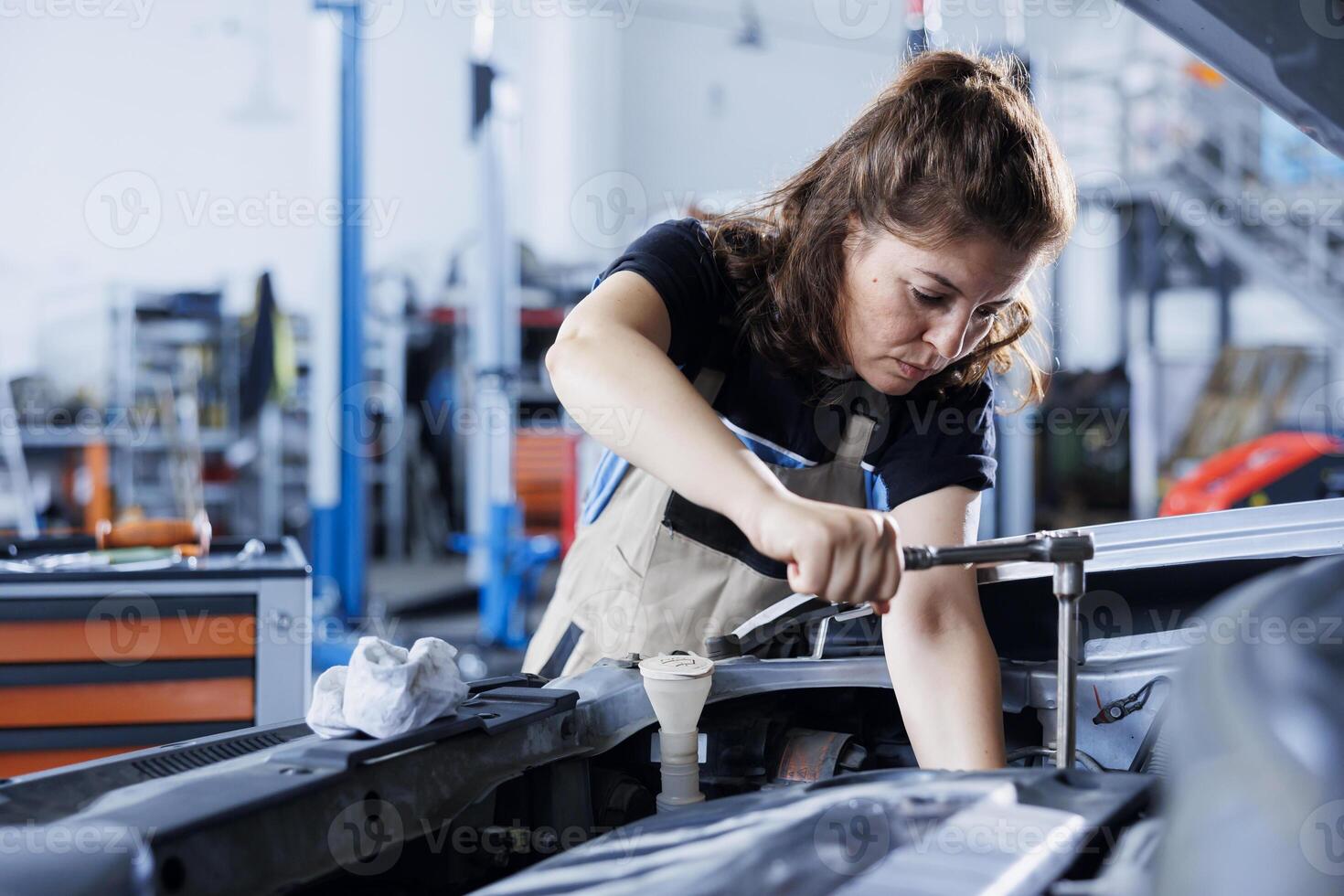Repair shop technician examines malfunctioning car battery using advanced mechanical tools, ensuring peak automotive performance. Employee in garage workspace conducts routine vehicle checkup photo