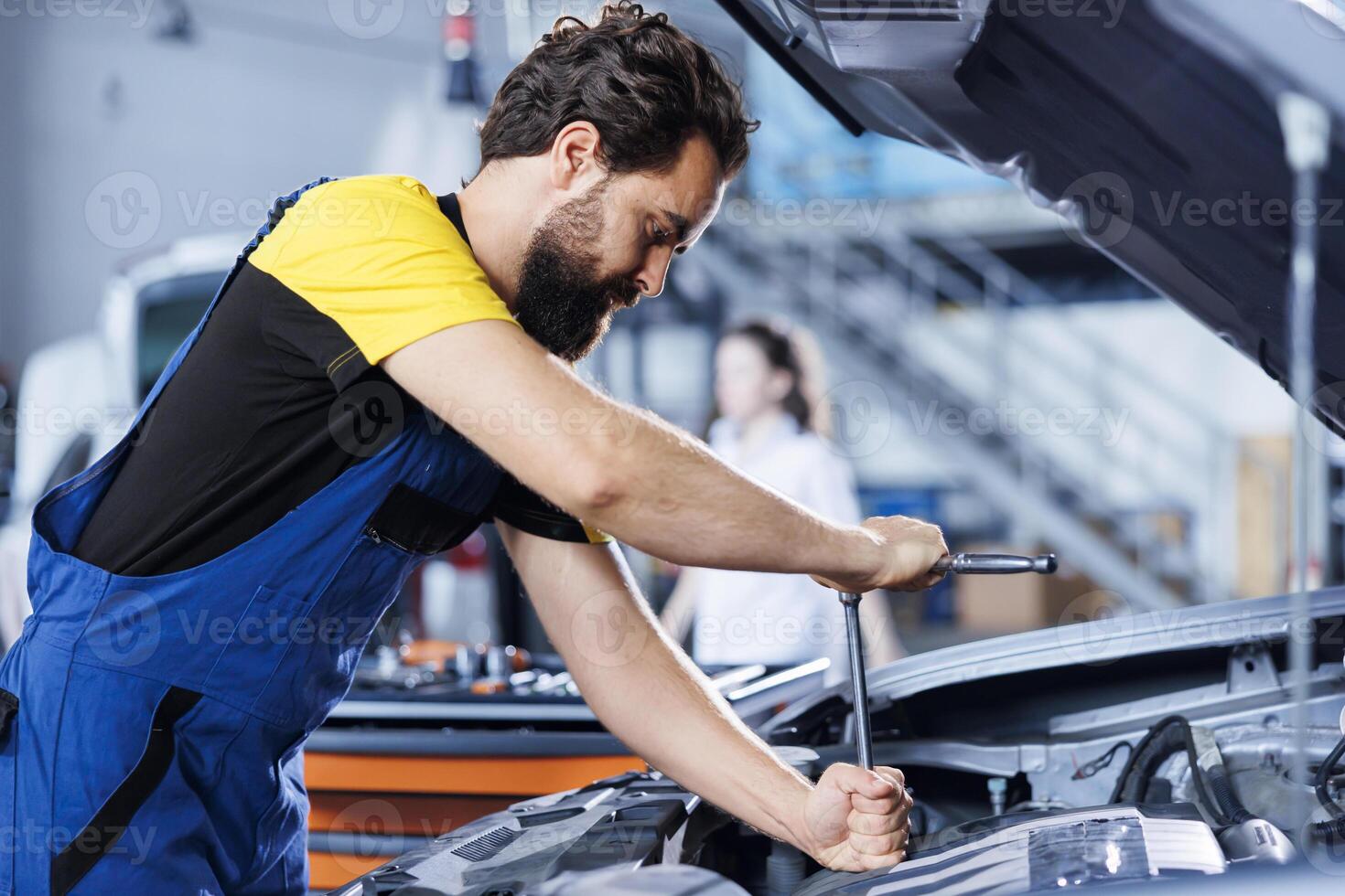Serviceman in car service picks torque wrench from work station bench, using it to tighten screws after replacing fuel tank. Meticulous garage worker uses professional tools to fix client automobile photo