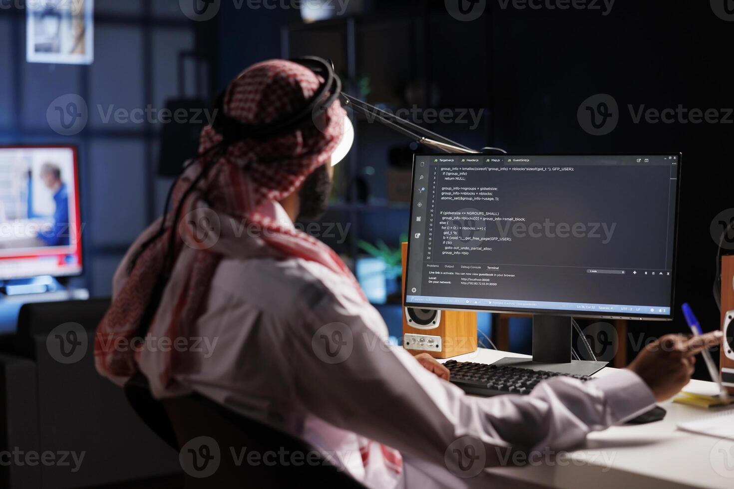 Islamic man shows how to design an app while sitting at desk and using a computer. Over-the-shoulder image of a pc monitor displaying active algorithms created by a traditional-dressed Arab guy. photo