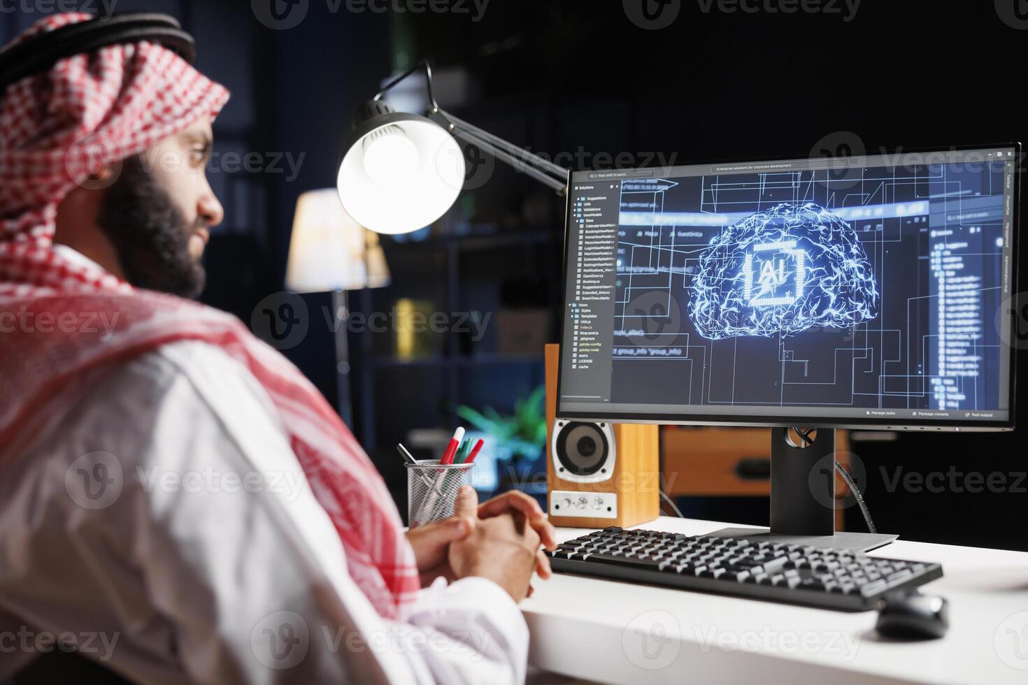Detailed image of Middle Eastern developer in front of desktop pc monitoring a complex network, ensuring data security and efficient computing using cloud, AI, and machine learning. photo