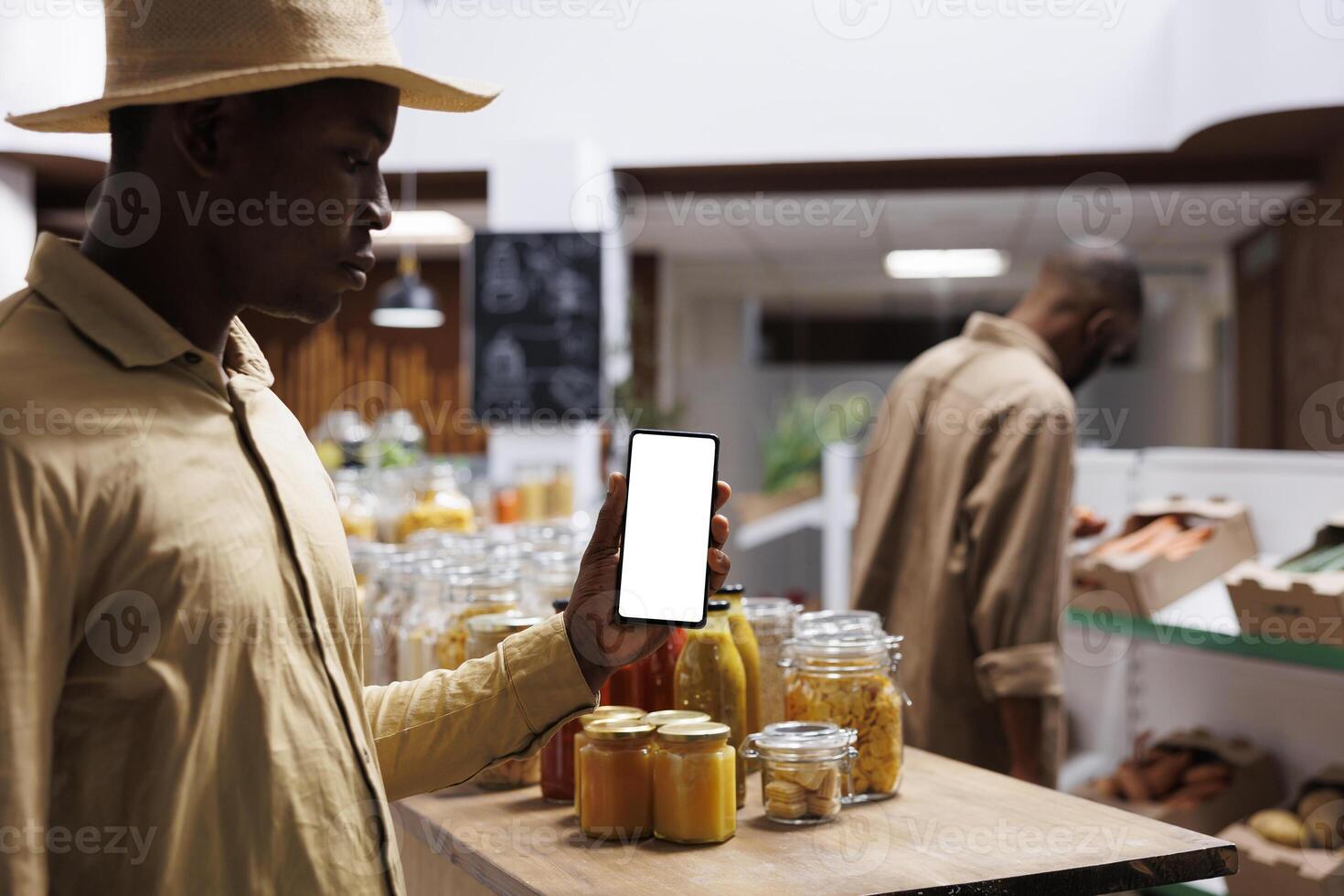 At an eco friendly grocery store, an African American male customer clutches a cell phone with an isolated white screen. The image shows a black man holding a mobile device with a chromakey template. photo