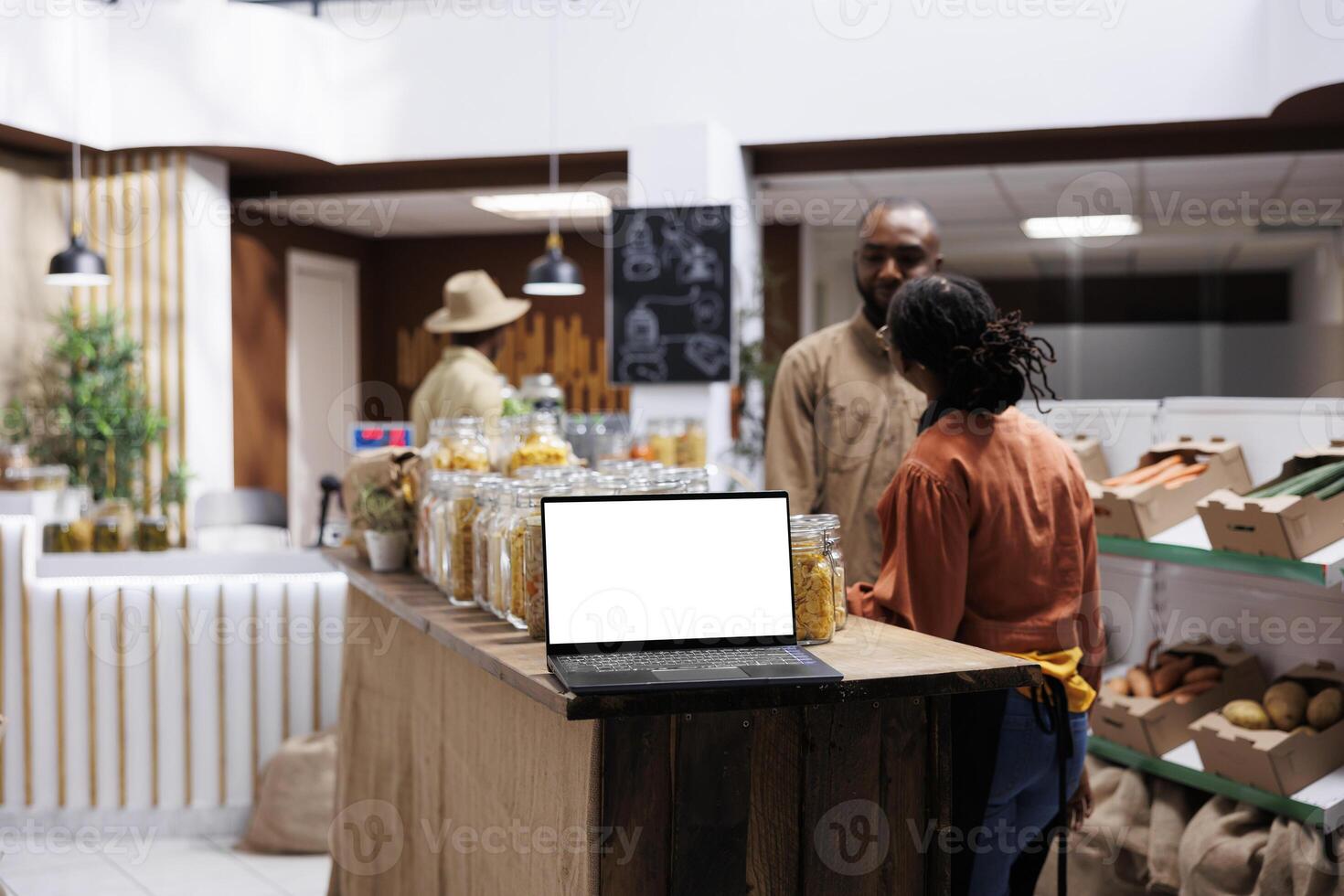 Placed on a wooden counter is a digital laptop showing an isolated white screen display. A wireless computer at a contemporary grocery shop has a blank chromakey mockup template. photo
